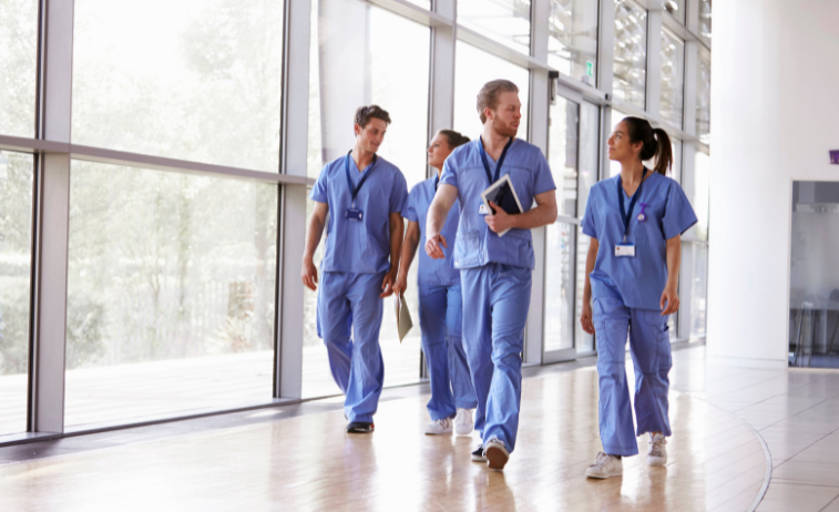four healthcare workers in blue scrubs walking down a hall and talking